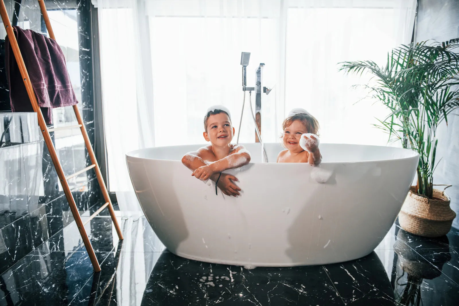 A luxurious bathroom with a white soaking tub, marble walls, and a crystal chandelier, showcasing elegant tub design.